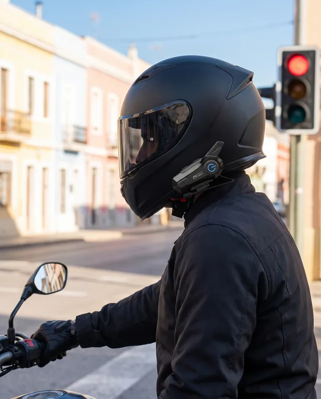 Motard arrêté à un feu rouge en ville en plein jour, main sur la poignée, boîtier visible sur le casque